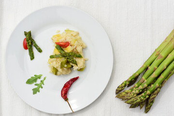 Risotto with green asparagus on a white plate, photographed from above on a white background, next to Greek green asparagus