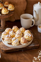 Homemade profiteroles with powdered sugar. Side view, wooden background.