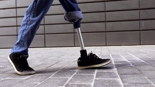 Young man with prosthetic leg walking on pavement
