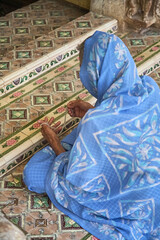 Woman with blue veil sits on the floor with a chain and prays. She belongs to the Hindu religion. Sitting in lotus position, she is in front of a tiled, beautiful temple entrance. Day. - obrazy, fototapety, plakaty