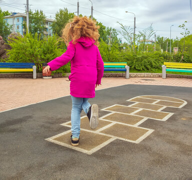 Redhead Girl Playing Hopscotch On School Playground. Back View. No Faces.