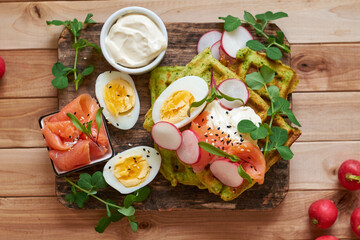 Spinach waffles with salmon, egg and radish. Top view, wooden background.