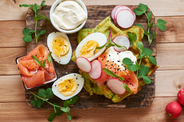 Spinach waffles with salmon, egg and radish. Top view, wooden background.