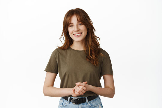 How may I assist you. Smiling friendly woman standing in pleasant formal pose, keeping emotions together, ready to offer help or assistance, standing against white background