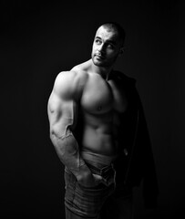 Obraz na płótnie Canvas Handsome pumped up brutal man with naked upper body in jeans and underwear standing showing muscles biceps and looking aside over dark background. Sport men body concept