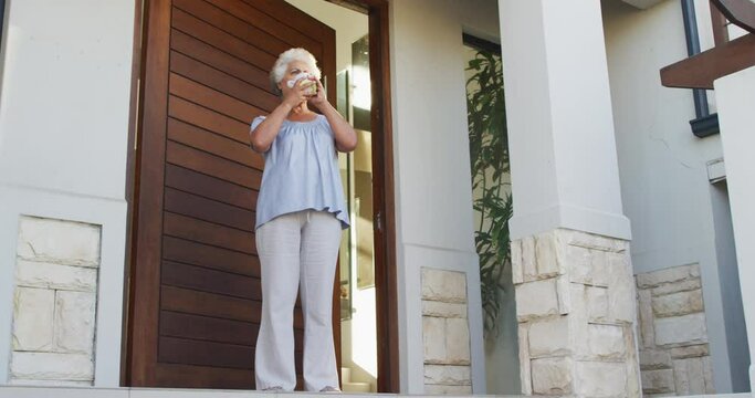 African american senior woman drinking coffee while standing at the front door at home
