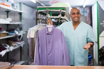 Positive man laundry worker returning clean clothes to customer at dry-cleaning facility