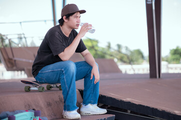 Young man rested to drink water after exhausting his skateboarding.