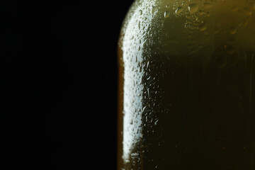 Wet bottle of beer against black background, close up