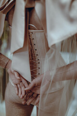 Female hands against the beige corset with lacing. Fashion shot