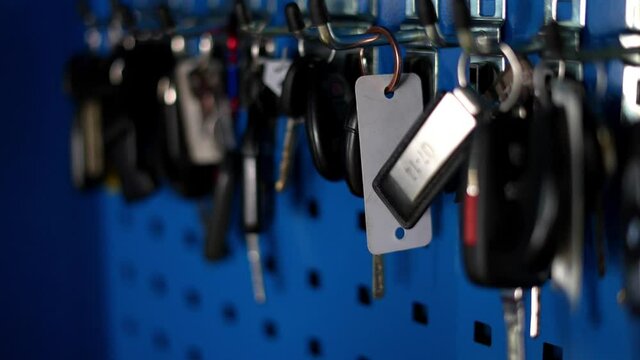 Lots of keys for cars trucks boats and other motorized toys hanging on bright blue key hook wall cubby area, in wealthy car guy motor head&rsquo;s garage. In 4k slow motion - shot on Sony A7Siii.