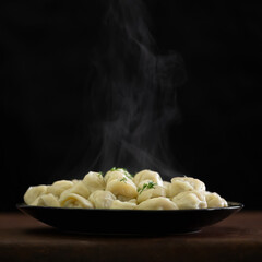 Pile of Hot cooked dumplings or ravioli sprinkled with dill. Plate with Convenience Food isolated on black background. Copy space on top of image. Soft focus. Dough stuffed. 
