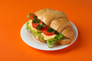 Plate with croissant sandwich on orange background