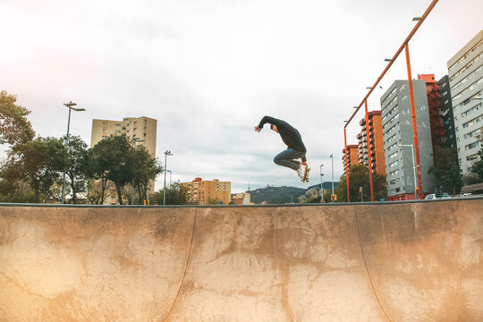 skater jumping high in the air with a snakeboard in a skatepark with white sky and buildings in the background with copyspace