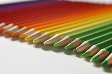 Fototapeta premium Multi-colored pencils of green-yellow-red shades lie on table