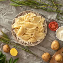 Pile of boiled dumplings with potatoes. Plate of delicious cooked food and ingredients for preparation on linen tablecloth. Traditional rustic dish. Dough stuffed. Convenience Food concept. Flat lay.