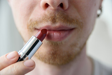 Bearded man applying red lipstick on his lips