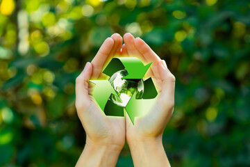 Save planet earth day concept. Female hands with recycle logo over green forest nature background....