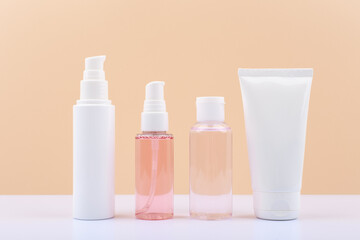 Set of cosmetic bottles for daily skin care. Face cream, cleaning foam, soothing lotion and exfoliating scrub against beige background.