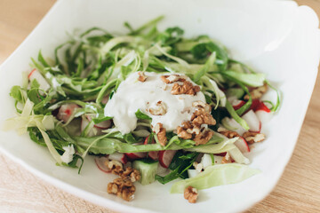 Summer vegetable salad chopped with fresh cabbage radishes, walnuts, sour cream on a white background 