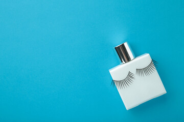 Perfume bottle with eyelashes on blue background