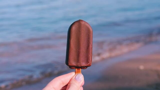 chocolate ice cream on stick in hands on the background of the sea in women's hand