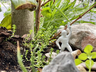 Closeup of a white figurine of a warrior on the soil surrounded by growing plants