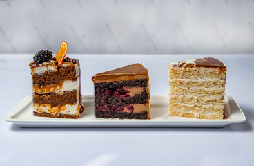 Three big slices of different sweet cakes on the white rectangular plate