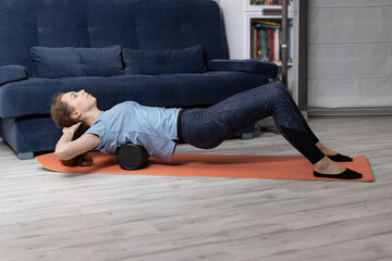 exercises for back with a gymnastic roller on the mat. Girl is engaged in stretching at home on the floor.
