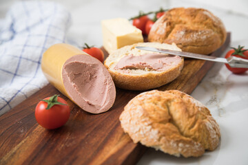 Feine Kalbsleberwurst auf Weizen Rosen Brötchen dazu Tomaten, Butter und Messer mit Holzbrett,...