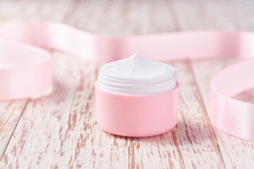 Natural face or body cream and pink silk ribbon on a white background.