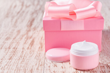 Natural moisturizer for sensitive skin and pink holiday gift box, on a wooden table.