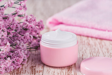 Obraz na płótnie Canvas Hygienic cream skincare product in pink plastic jar with towel on white table.