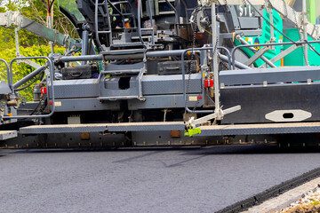 Asphalt paver on the road while laying asphalt, part of the car close up. Road repair. Laying a new road