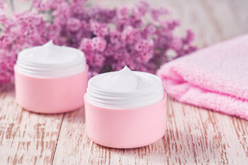 Fototapeta na wymiar Natural face cream or lotion, organic cosmetic product to moisturize the skin with a towel and flowers on the background. Pink series cosmetic.