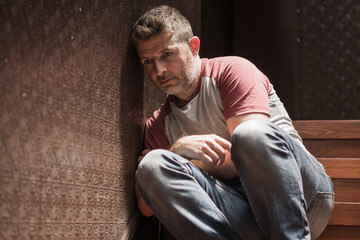 unemployment and divorce - dramatic lifestyle portrait of sad and depressed man on his 40s sitting indoors on staircase thoughtful and worried suffering depression problem