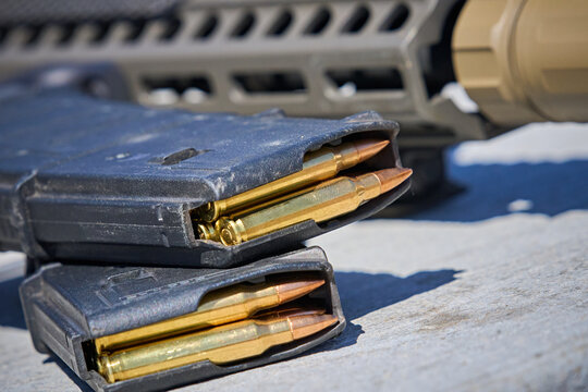 AR15 Rifle Magazines stacked sitting next to an AR15 carbine rifle on a table at an outdoor shooting range. 