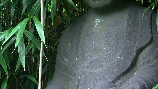 Tilt up from hands to face of statue of Jizo in a Japanese garden.