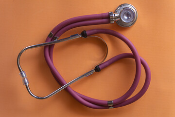Red stethoscope, equipment to examine respiration and heartbeat. Orange background.