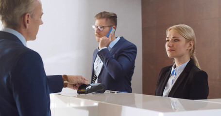 Smiling female receptionist taking payment with credit card from mature businessman