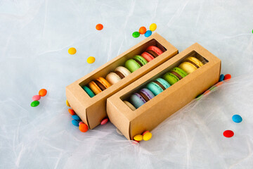 Multicolored macarons in a paper box and multicolored sweets on a romantic background.