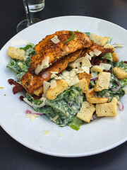 Ceasar salad on white plate served in restaurant. Fried chicken breast, bred croutons, parmesan chesse and lettuce.