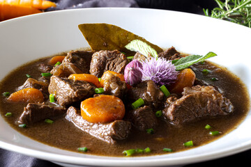 beef ragout stew with carrots, vegetables and greens on black background