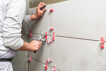 Tiler placing ceramic wall tile in position over adhesive with lash tile leveling system