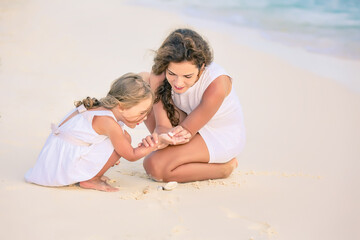 Mother with little daughter playing on ocean beach, Maldives. Family on the beach concept.
