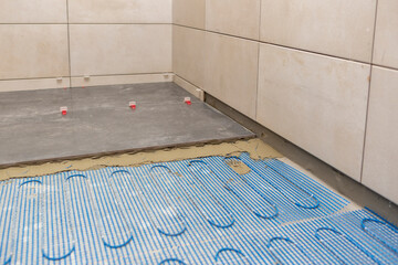 Renovation and improvement concept, Installing a floor heating system under ceramic tiles in bathroom