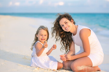 Mother with little daughter playing on ocean beach, Maldives. Family on the beach concept.