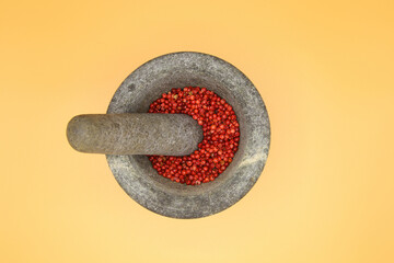 Top view close up on isolated gray basalt stone mortar with pestle and red pepper corns, yellow blank background (focus on center)