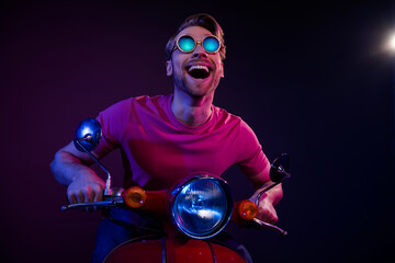 Portrait of attractive amazed cheerful guy riding bike having fun isolated over dark neon purple...