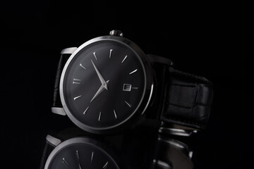A luxury men's watch with a black leather strap, on a reflective surface